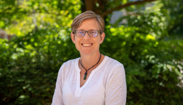 A woman with short hair and glasses, smiling. Outside.