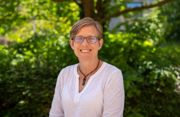 A woman with short hair and glasses, smiling. Outside.