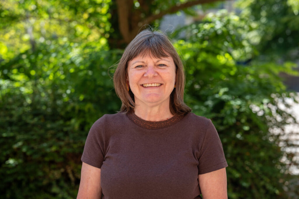 A woman with short brown hair wearing a brown top, smiling. Outside.