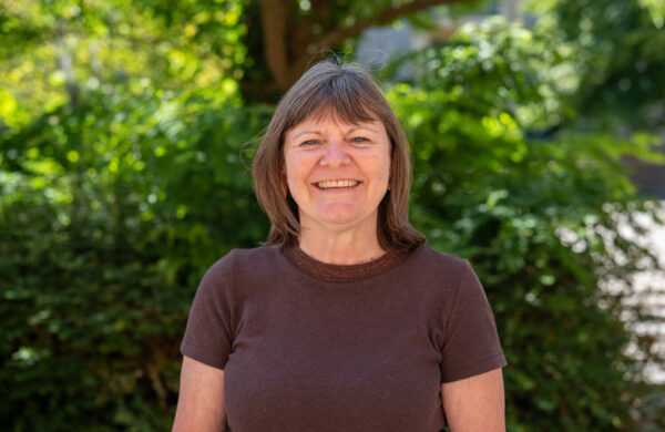 A woman with short brown hair wearing a brown top, smiling. Outside.