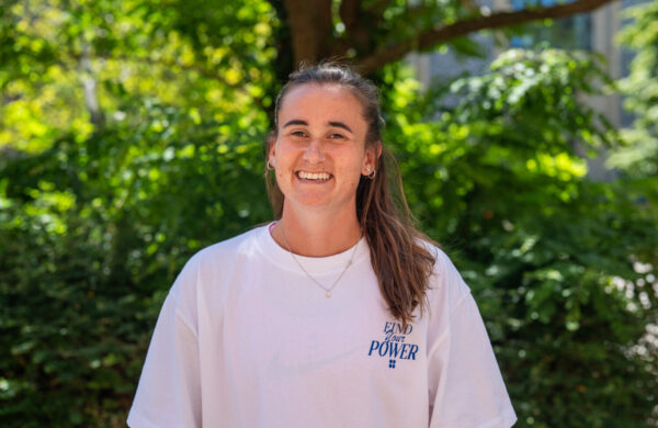 A woman with brown hair wearing a white top, smiling. Outside.
