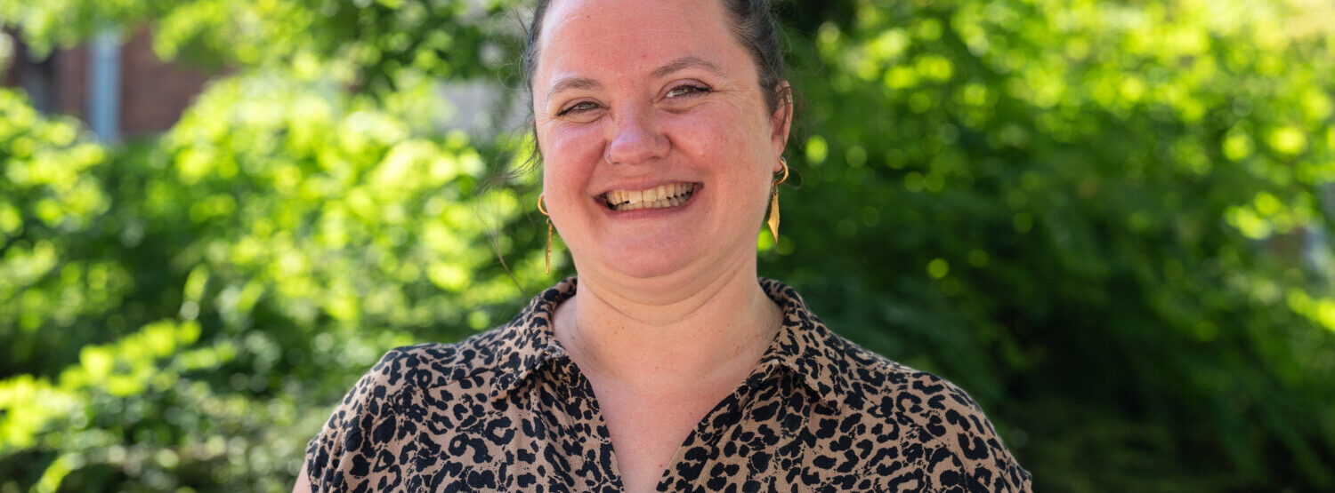 A woman in leopard print dress, smiling. Outside.