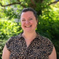 A woman in leopard print dress, smiling. Outside.