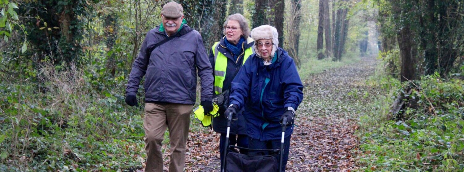 Three people on a health walk - one with a walking aid