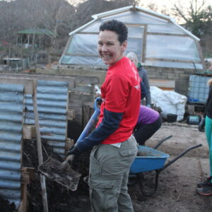 Smiling volunteer wearing red GoodGym t-shirt and holding a shovel full of compost.