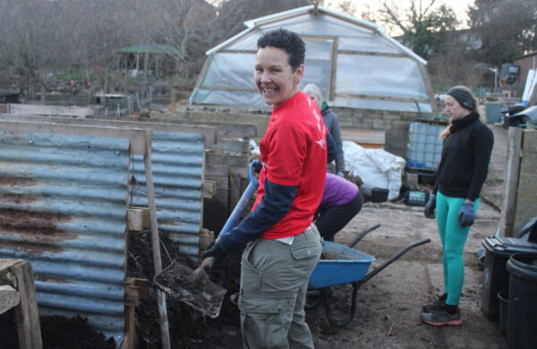 Smiling volunteer wearing red GoodGym t-shirt and holding a shovel full of compost.