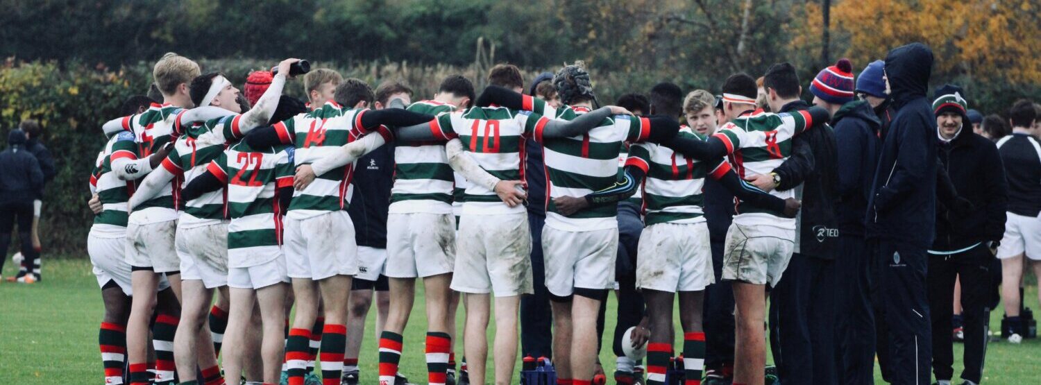 A rugby squad huddled on the pitch.