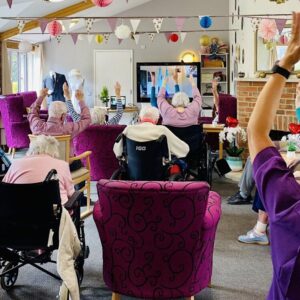 A group of older people taking part in chair based exercise in a care envrionment.