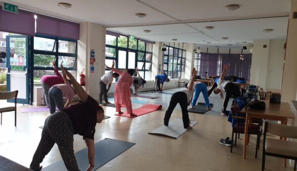 A group of people stretching on mats in a hall full of windows to one side. They're bending over to touch their toes.