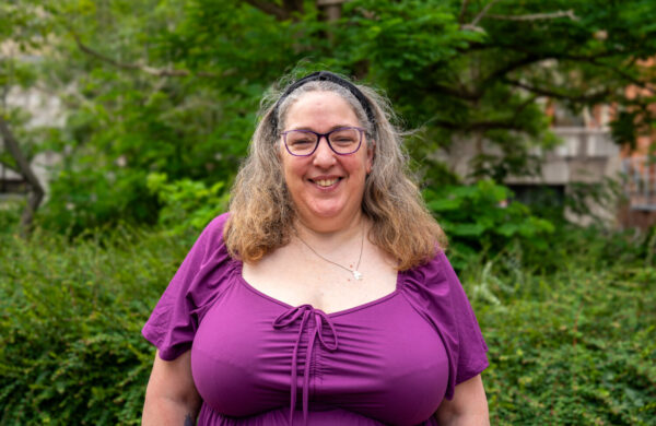 A woman wearing glasses and a purple top, smiling. Outside.