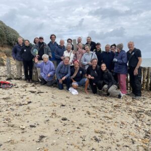 A group of 25 people from Dementia Friendly Alton, smiling at he camera at Lepe Beach, New Forest.