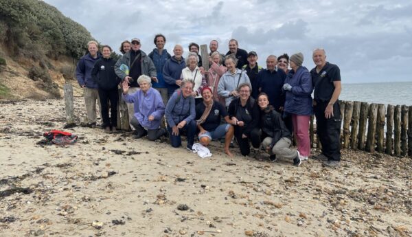 A group of 25 people from Dementia Friendly Alton, smiling at he camera at Lepe Beach, New Forest.