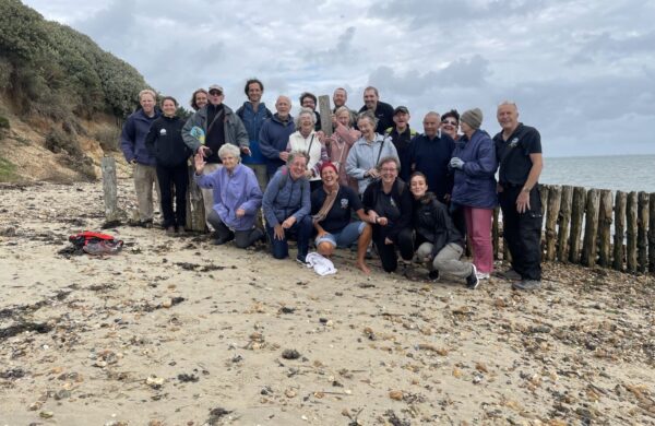 A group of 25 people from Dementia Friendly Alton, smiling at he camera at Lepe Beach, New Forest.