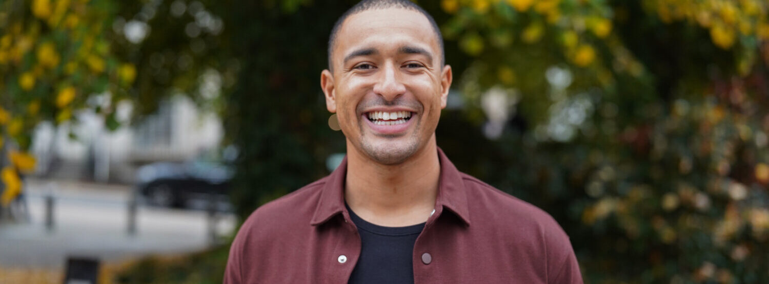 A man in a burgundy shirt, smiling, outdoors.