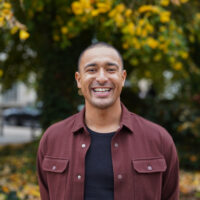 A man in a burgundy shirt, smiling, outdoors.