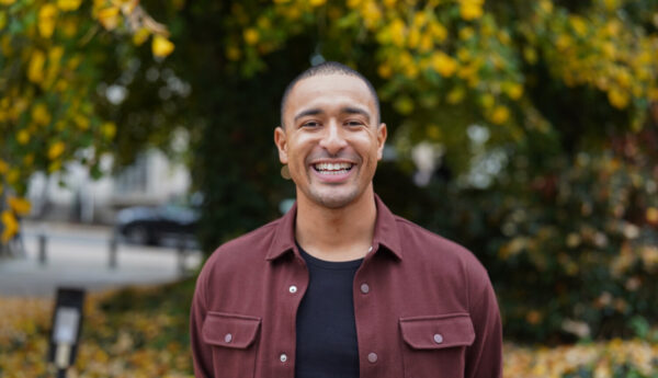 A man in a burgundy shirt, smiling, outdoors.