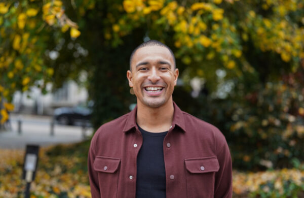 A man in a burgundy shirt, smiling, outdoors.