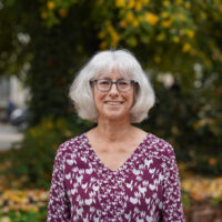 A woman in a purple blouse, wearing glasses, outside.