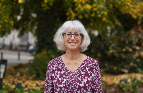 A woman in a purple blouse, wearing glasses, outside.