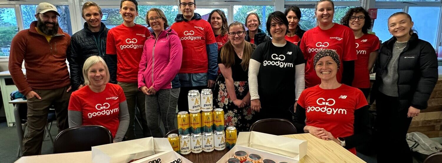 A group of people smiling and facing the camera. They are wearing Good Gym red t-shirts. There are cupcakes on the table in front of them.