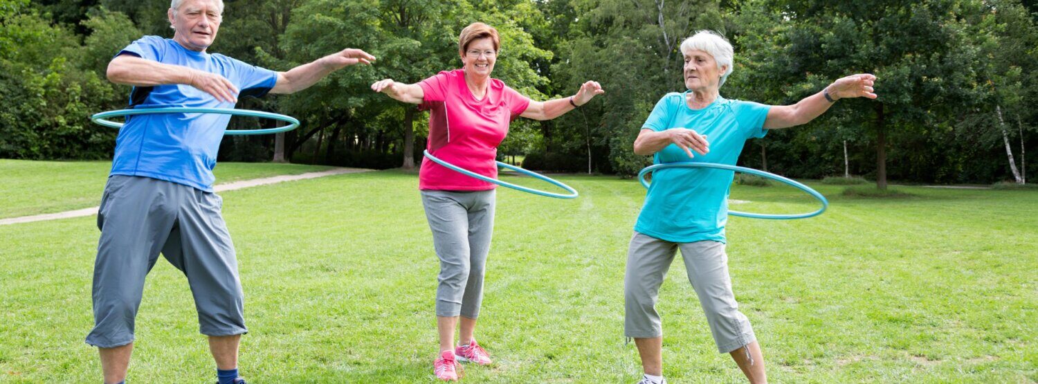 Three older adults hoola hooping in the park.