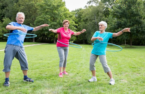 Three older adults hoola hooping in the park.