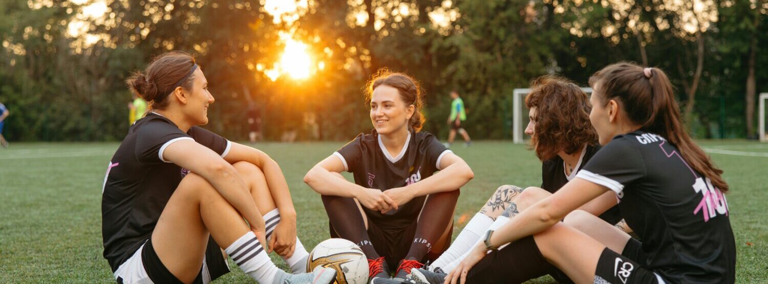 Four girls sat on the grass with a football in the centre of them.