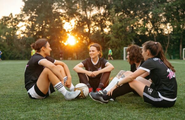 Four girls sat on the grass with a football in the centre of them.