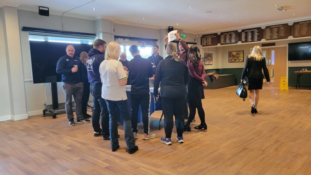 A group of people with their backs to the camera, gathering around a man holding a discussion topic sign.