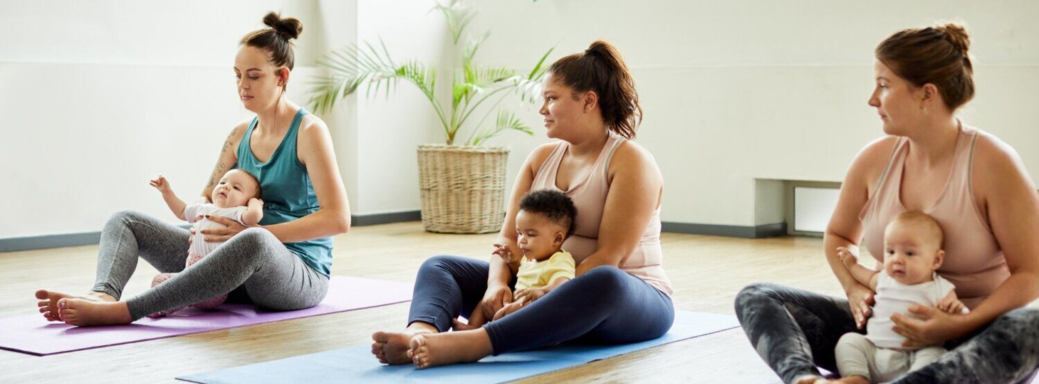 Three Mums with their babies in their laps sitting on yoga mats.
