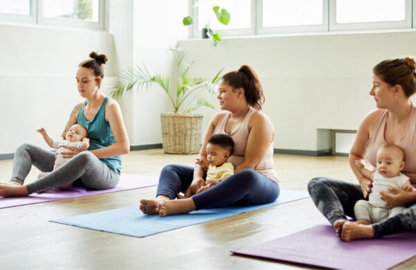 Three Mums with their babies in their laps sitting on yoga mats.