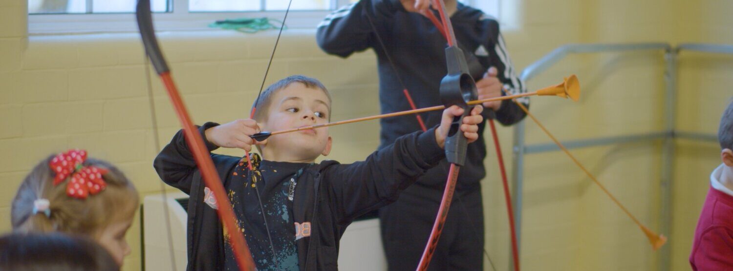 A young boy pulling his arrow back, holding a bow.