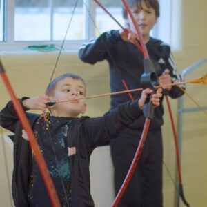 A young boy pulling his arrow back, holding a bow.