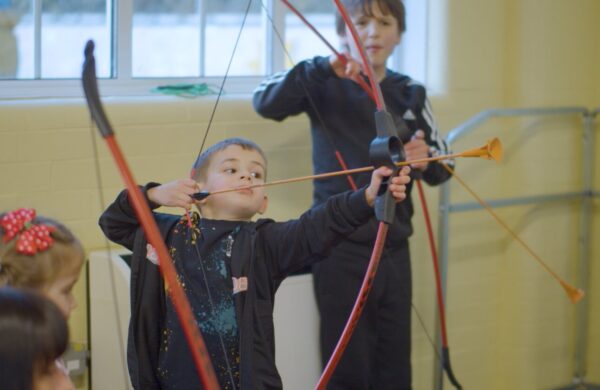A young boy pulling his arrow back, holding a bow.