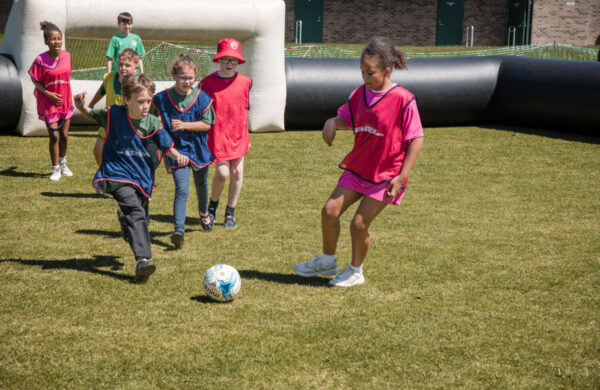A group of young children playing football on a summer's day.