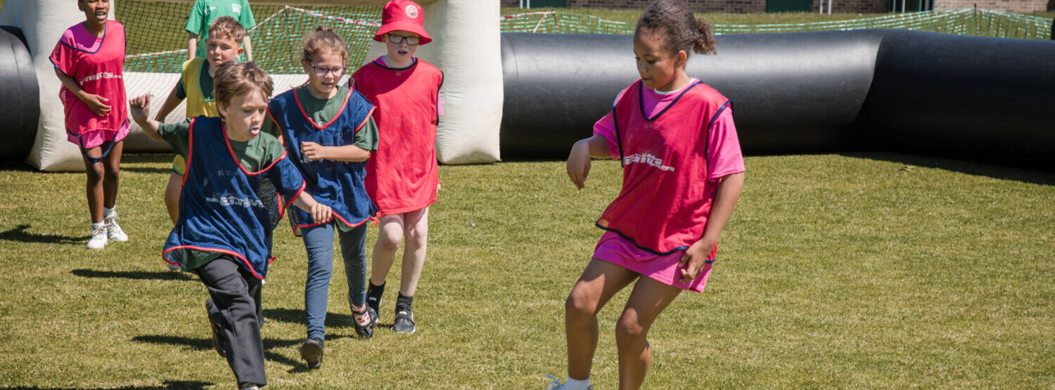 A group of young children playing football on a sunny day.