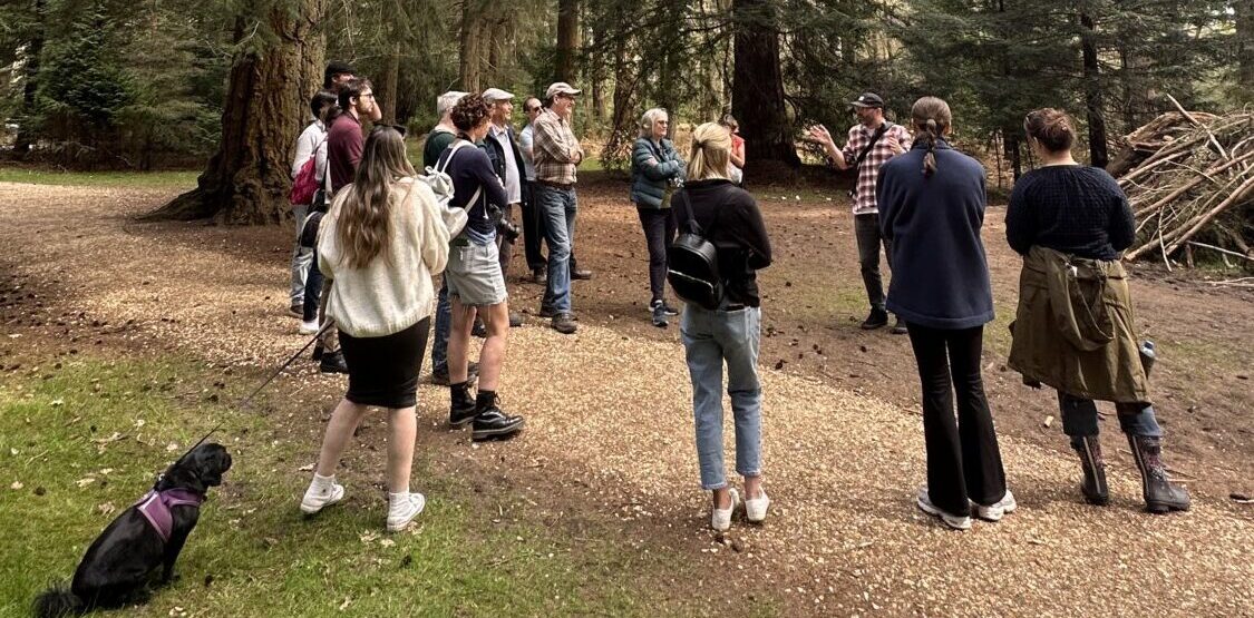 A group of people in a woodland listening to the group leader speak.