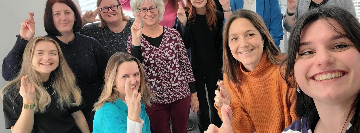 A group of people smiling at the camera holding their fingers crossed like the national lottery logo