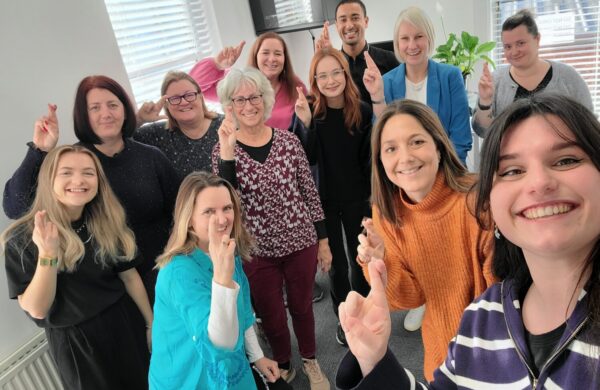 A group of people smiling at the camera holding their fingers crossed like the national lottery logo