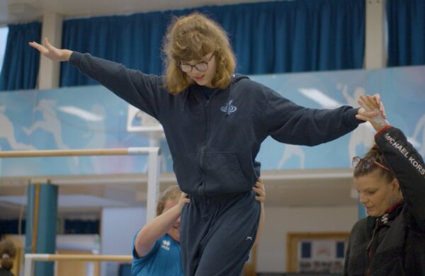 A young girl being assisted across a balance beam.