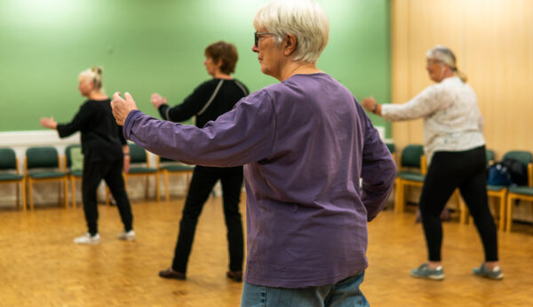 A tai chi class. An older woman in a purple top is in the foreground.