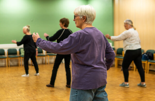 A tai chi class. An older woman in a purple top is in the foreground.