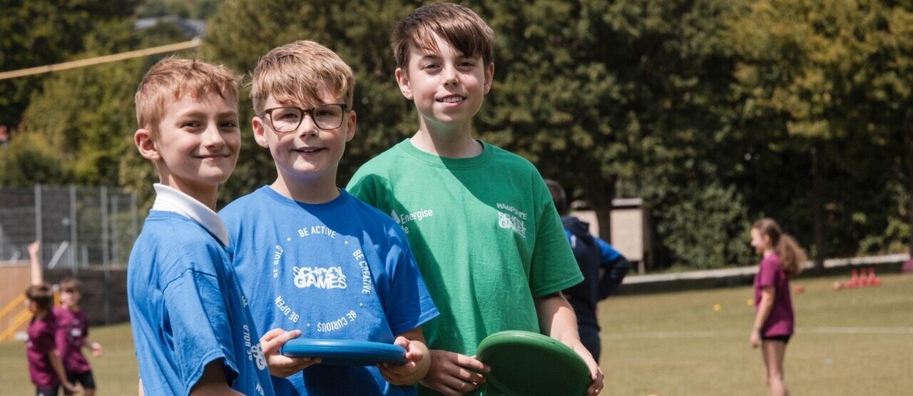 three young boys smiling at the camera. They are holding frisbees