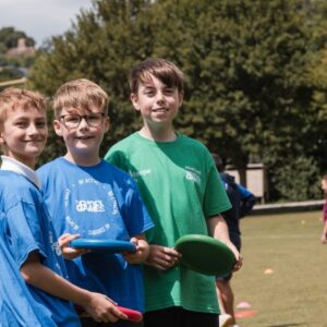 three young boys smiling at the camera. They are holding frisbees