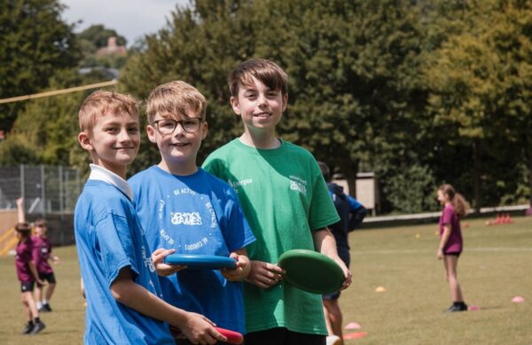 three young boys smiling at the camera. They are holding frisbees