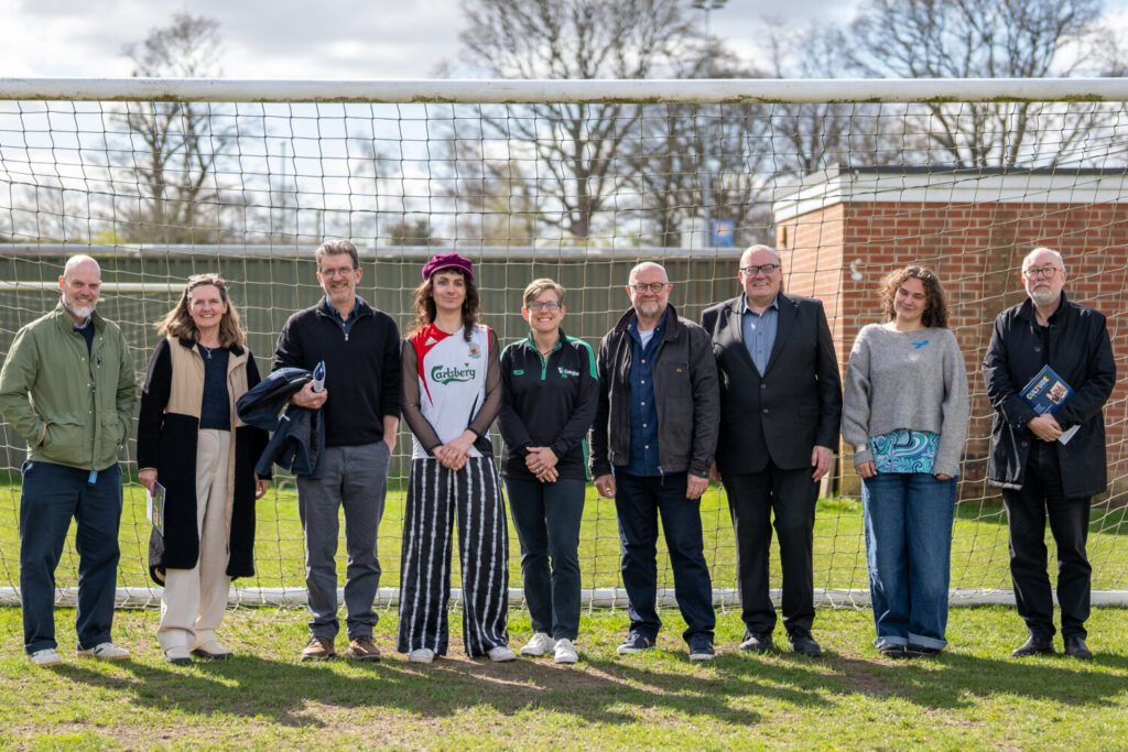 A line of people stood in front of a goal post on a pitch.