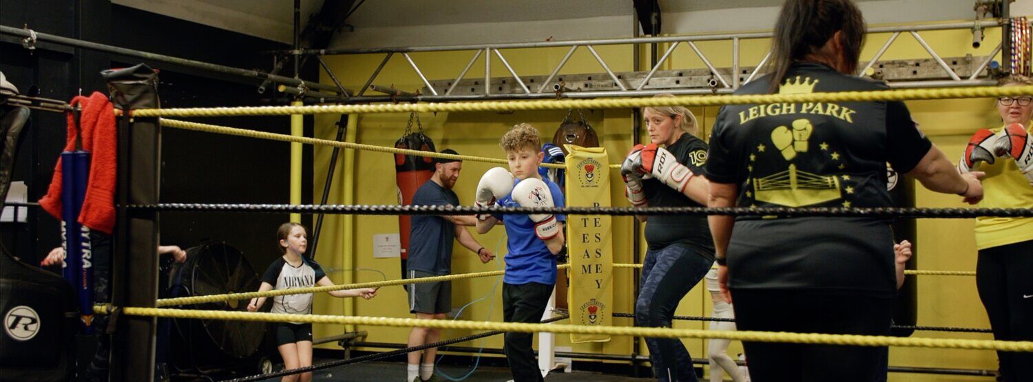 A child and parent in a boxing ring, in a training stance. They are taking part together