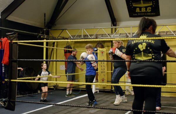 A child and parent in a boxing ring, in a training stance. They are taking part together