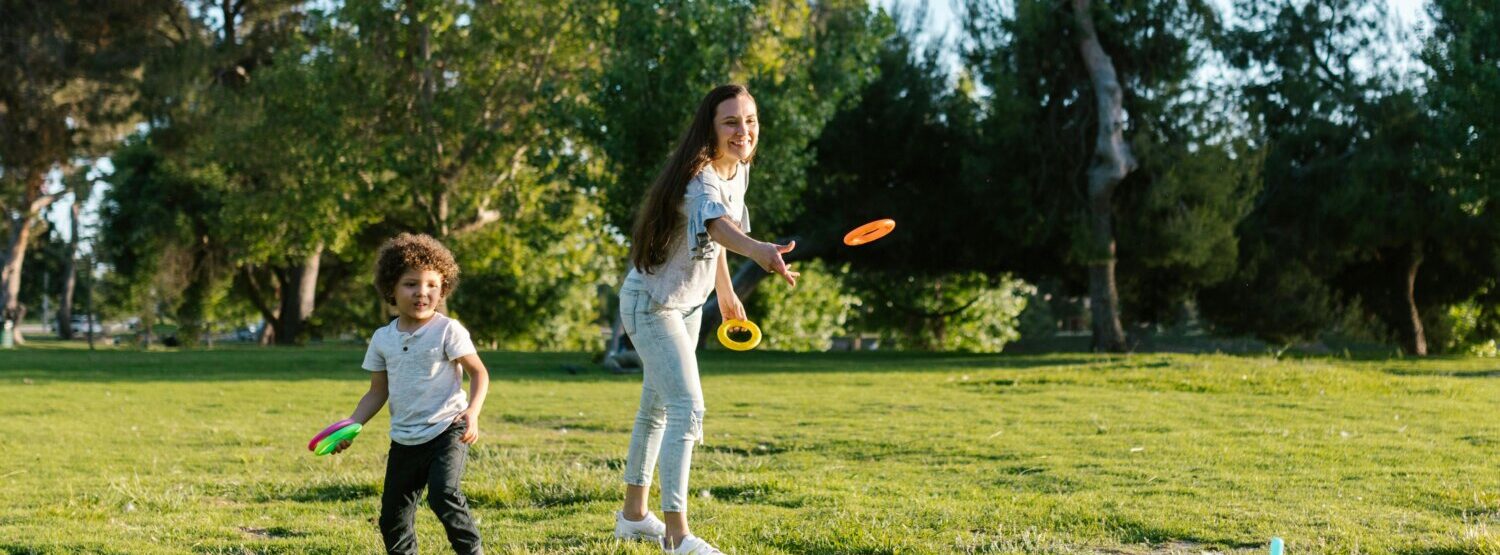 A mother and son throwing hoops onto sticks in the park.