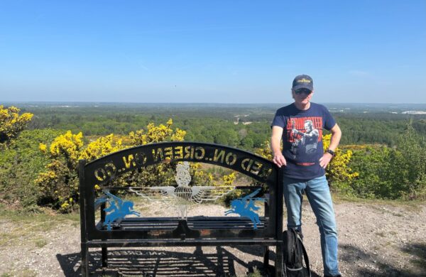 A man stood beside a bench overlooking a valley.